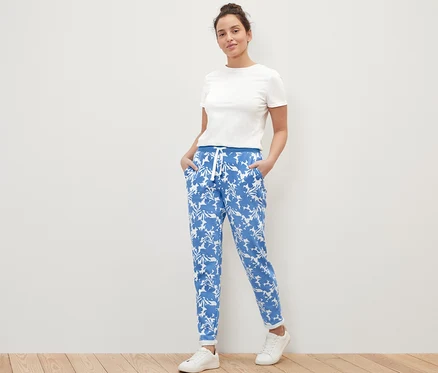 Eine Frau posiert in bedruckten Sweatpants, einem weißen T-Shirt und Turnschuhen.
