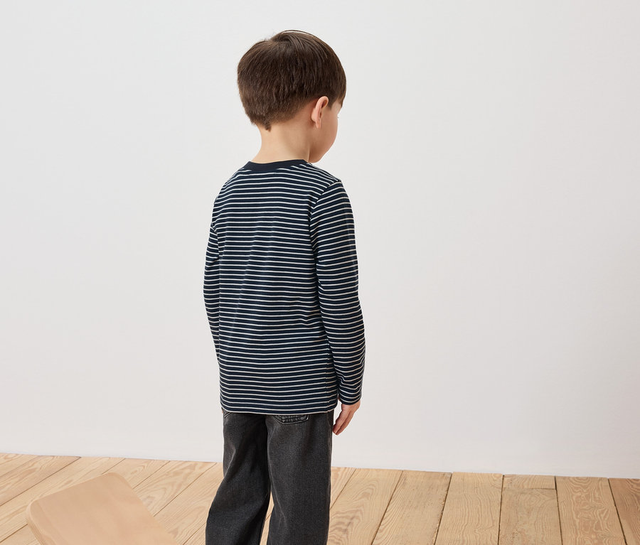 Ein Junge steht mit dem Rücken zur Kamera und trägt ein gestreiftes Langarmshirt und Jeans.