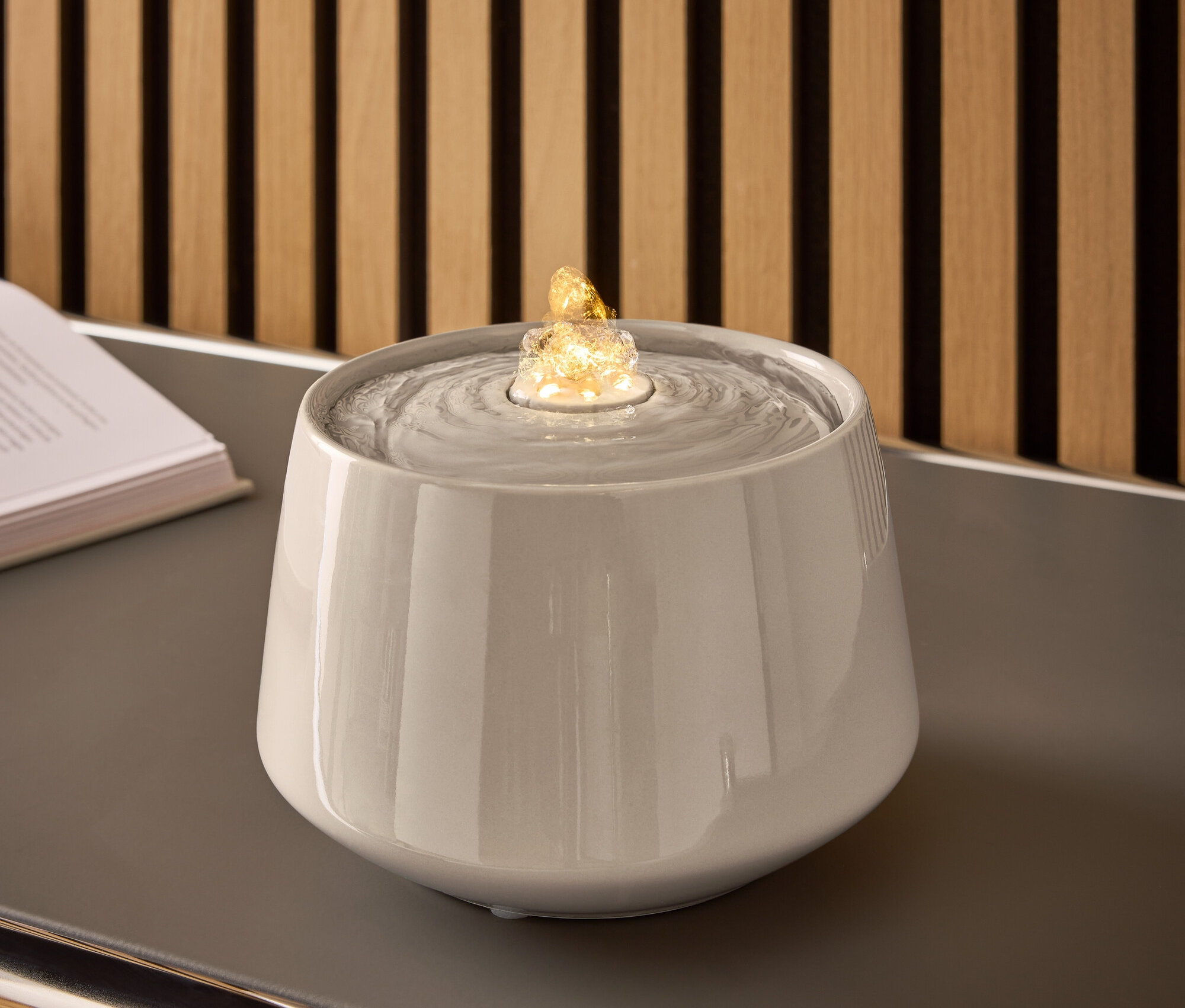 Grauer Keramikbrunnen mit Wasser und beleuchtetem Stein auf einem grauen Tisch.