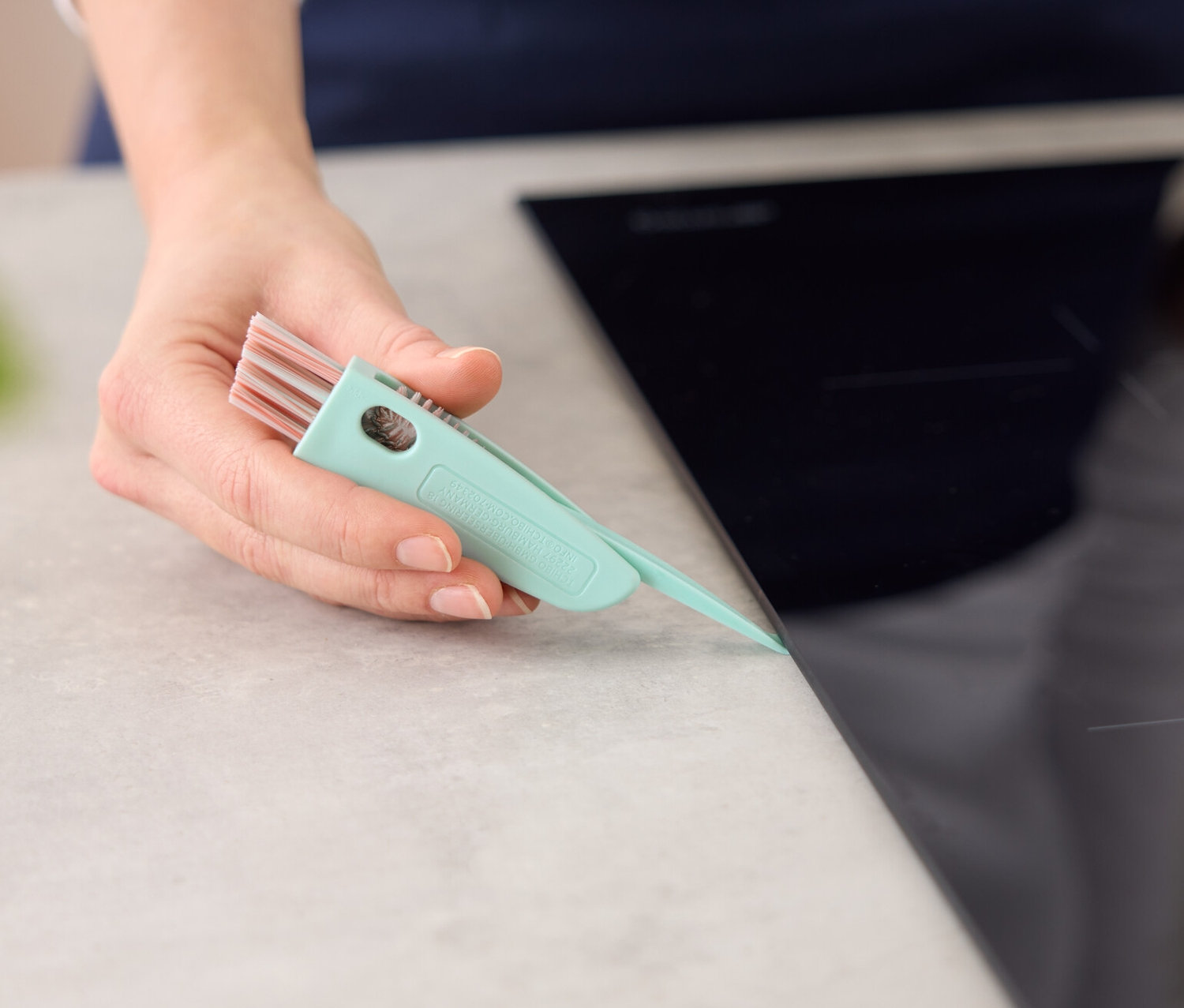 Frau reinigt den Rand eines Kochfelds mit einer 3-in-1-Reinigungsbürste.