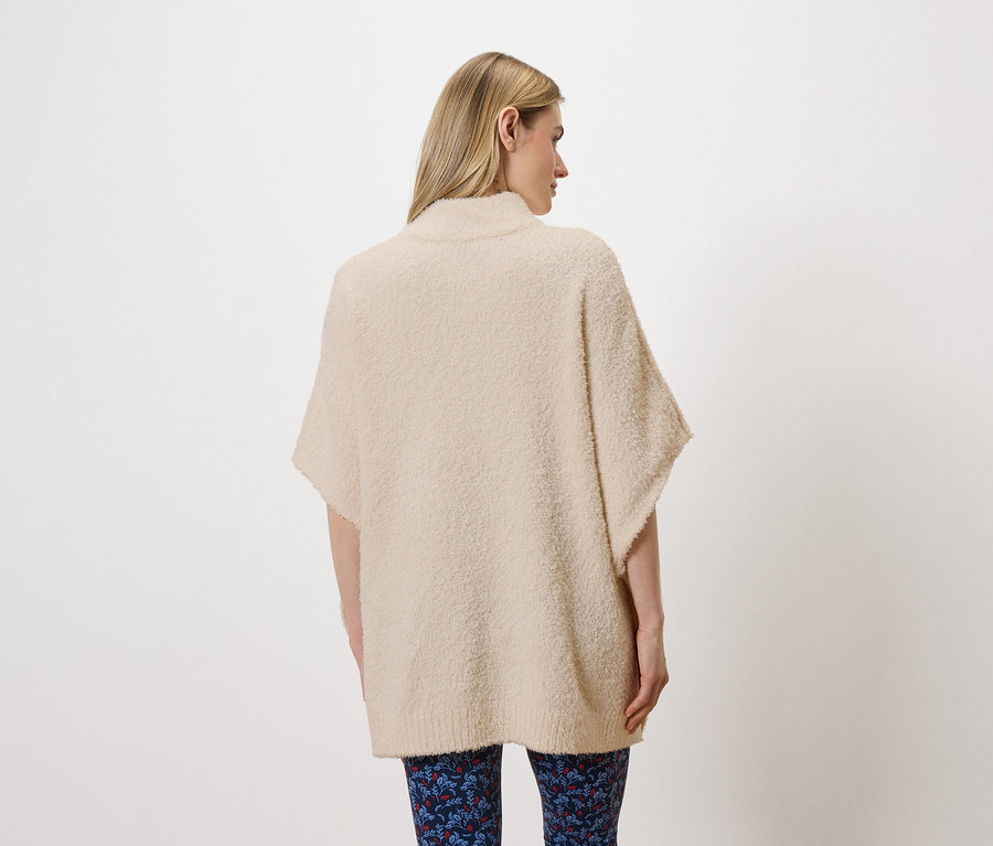 Eine Frau steht mit dem Rücken zur Kamera und trägt einen beigen, kurzärmeligen Pullover und blaue Leggings mit Blumenmuster.
