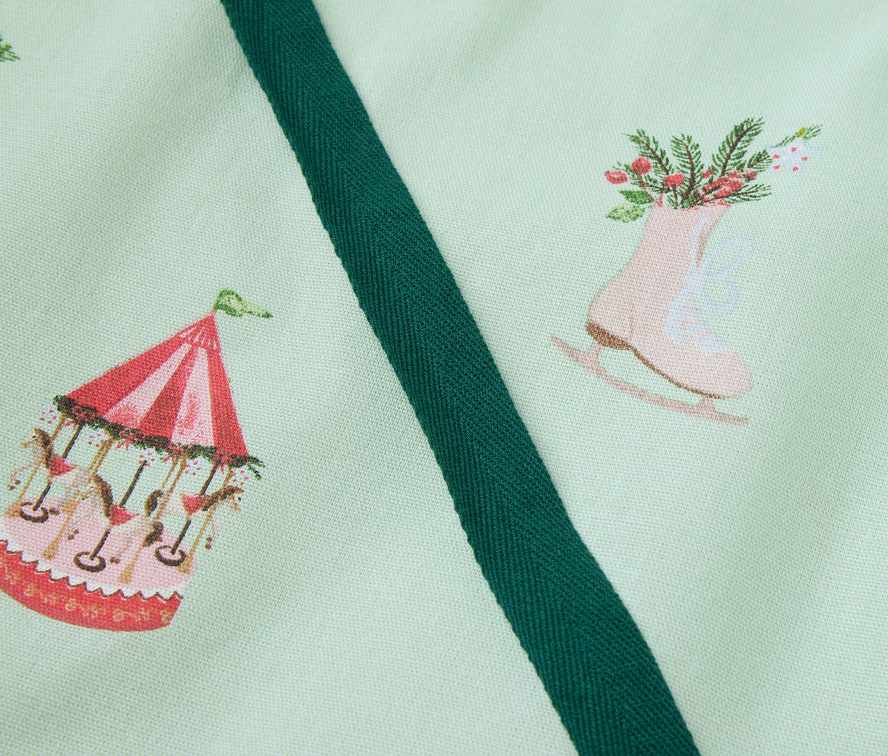 Hellgrüner Stoff bedruckt mit Karussell, Schlittschuhen mit Blumen und Lebkuchenhaus.
