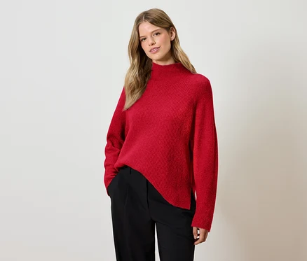 Frau posiert in rotem Pullover und schwarzer Hose.