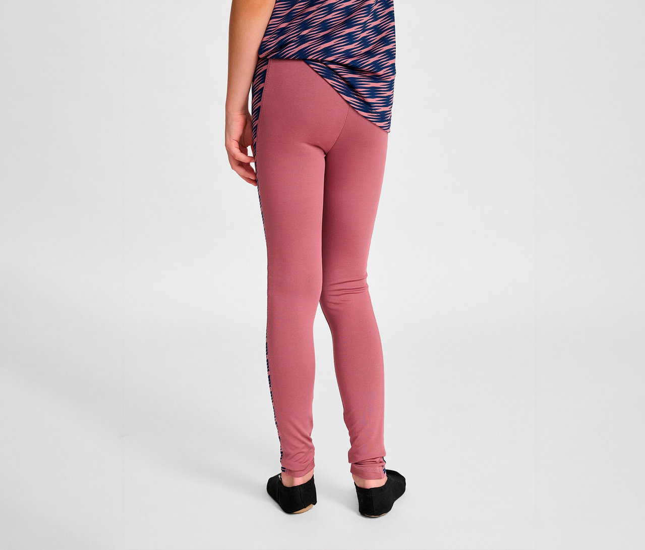 Rückansicht eines Kindes, das rosafarbene HUMMEL HMLJR Mix Mid Waist Tight Leggings und ein blau-weißes T-Shirt trägt.