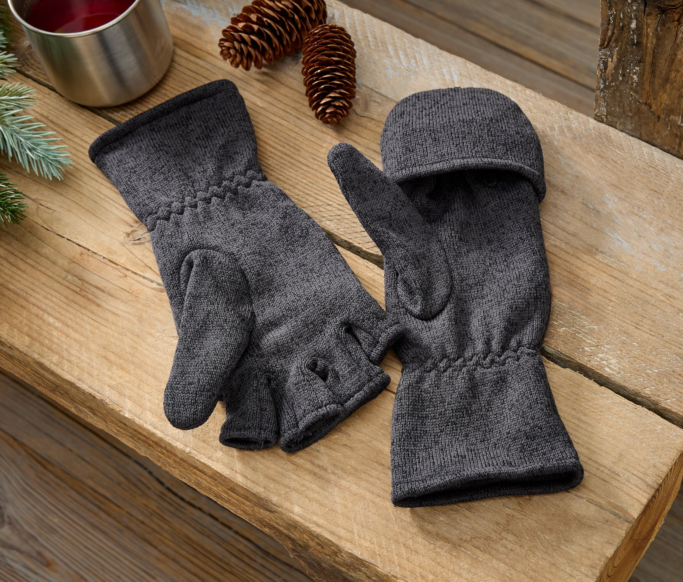 Zwei graue Fausthandschuhe liegen nebeneinander auf einer Holzbank.