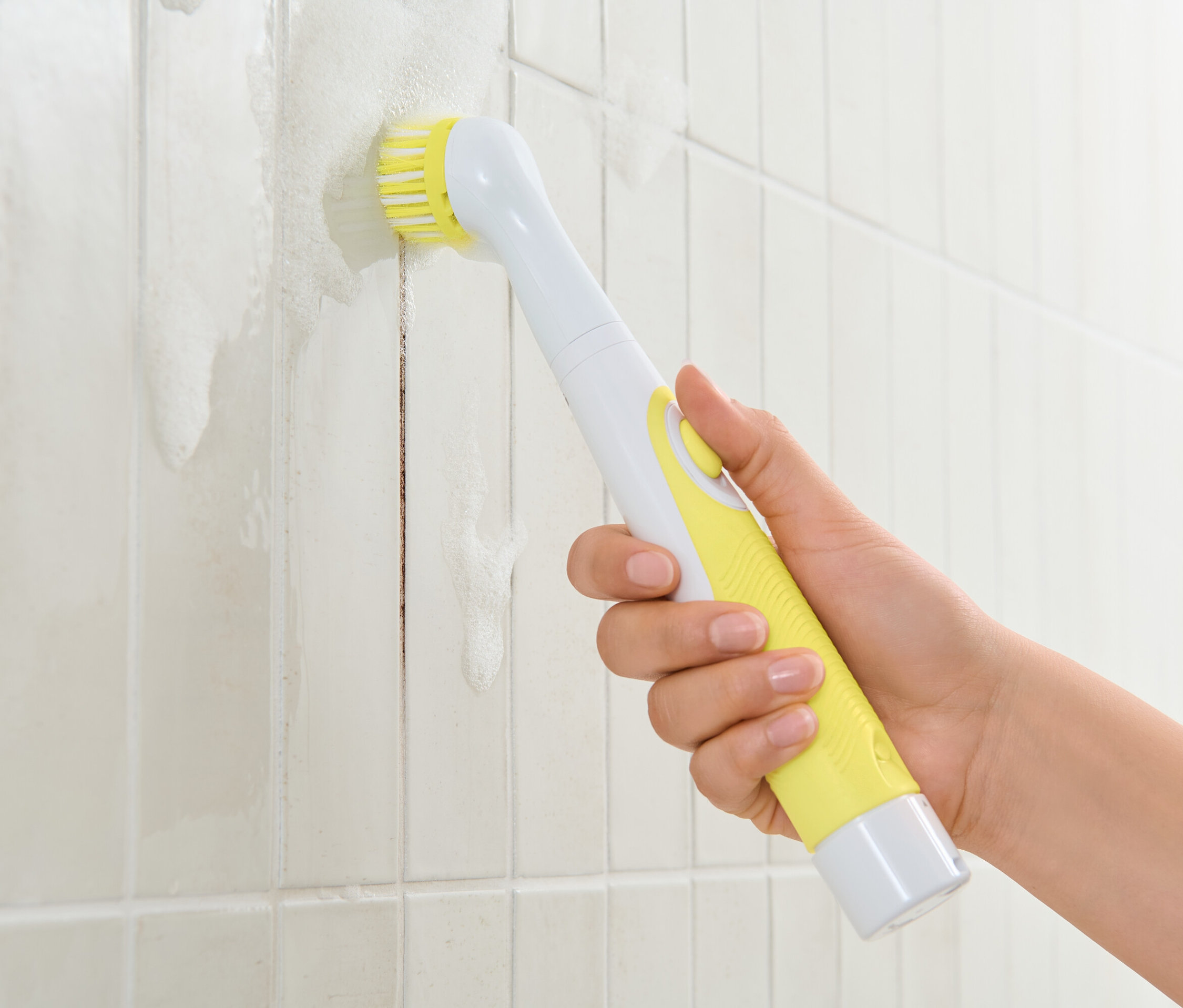 Eine Hand hält eine elektrische Reinigungsbürste mit gelbem Griff und reinigt weiße Fliesen
