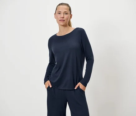 Frau in marineblauem Pullover und Hose posiert vor einem weißen Hintergrund.