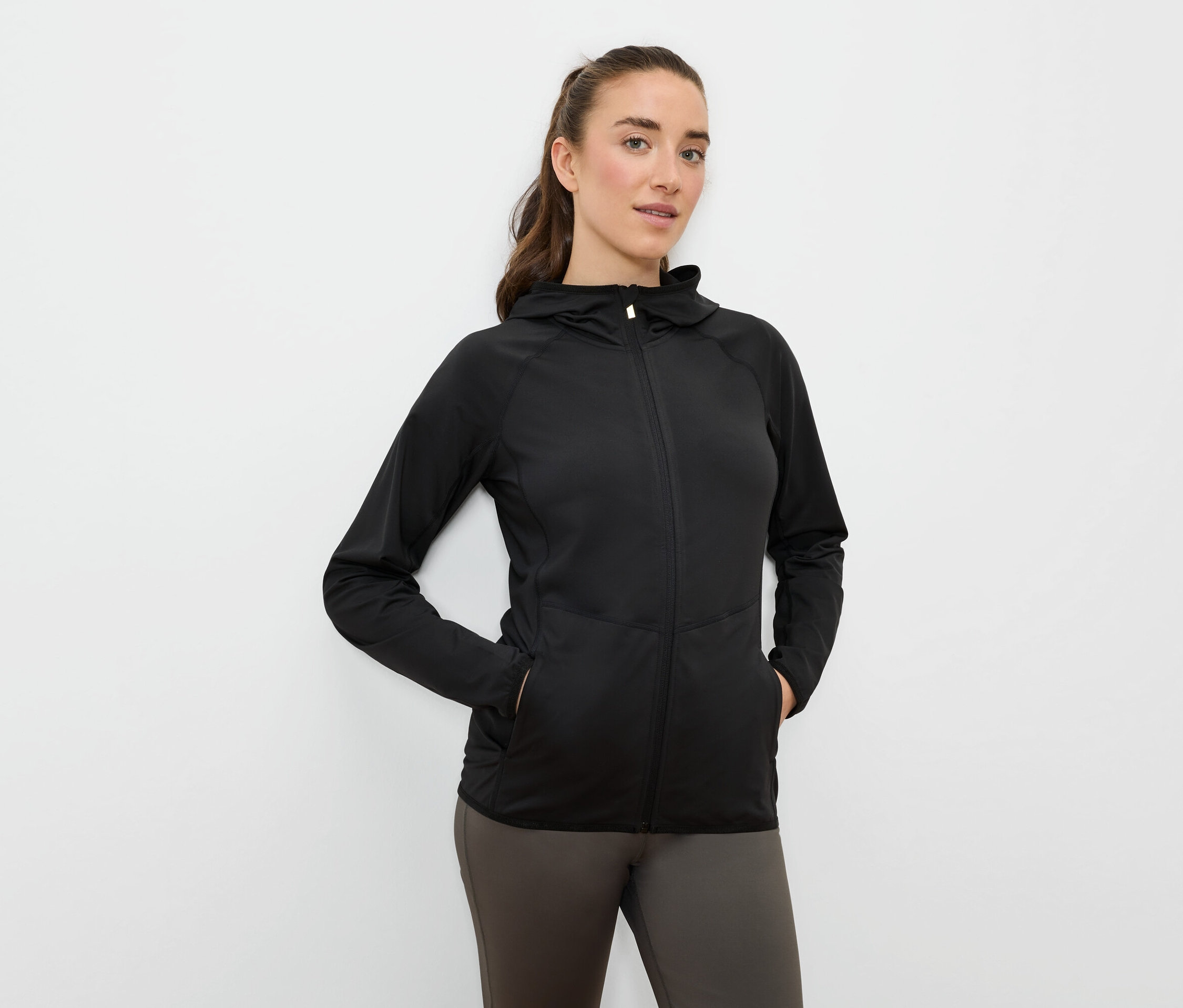 Frau mit Händen in den Taschen einer schwarzen Sportjacke mit Kapuze und Reißverschluss.