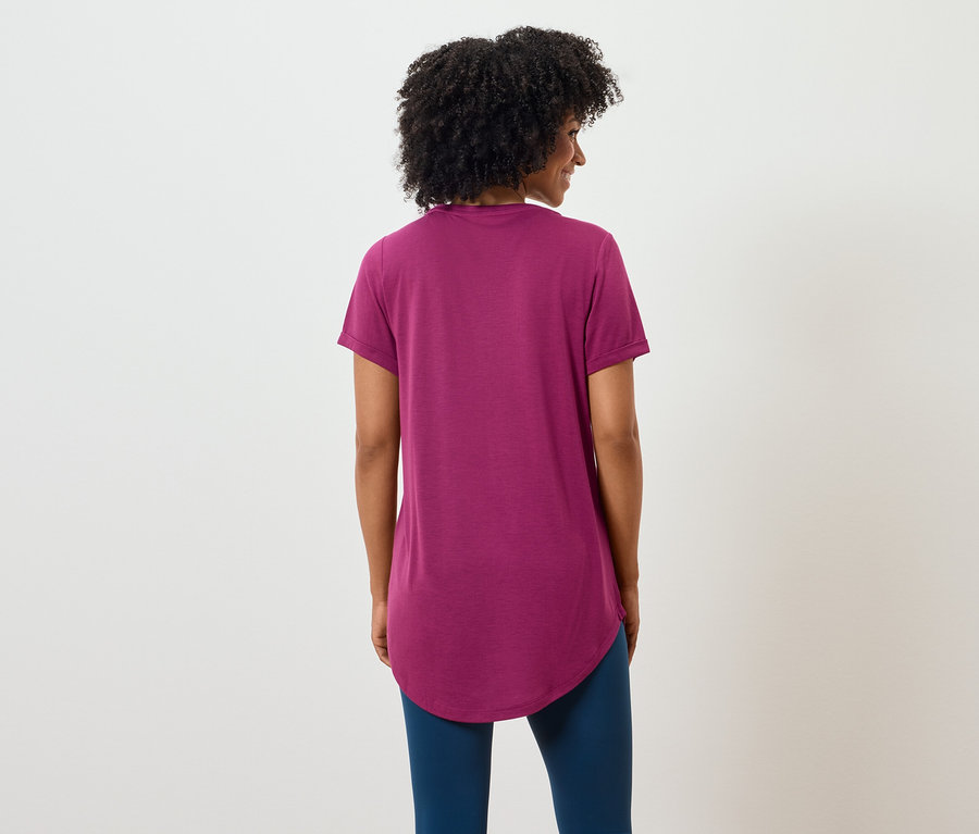 Rückansicht einer Frau mit dunklen lockigen Haaren, die ein purpurrotes T-Shirt und blaue Leggings trägt.