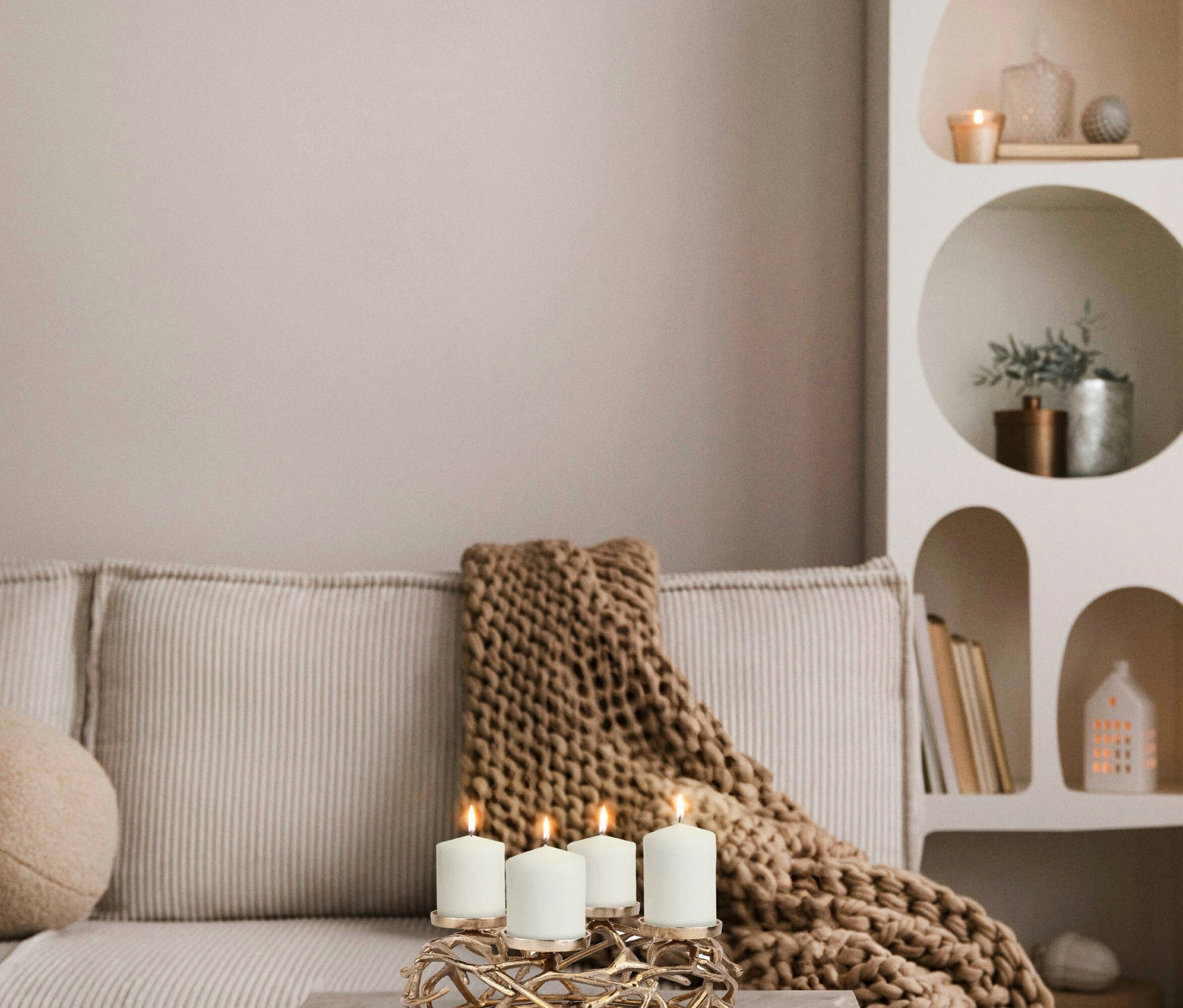 Vier weiße Kerzen brennen in einem dekorativen goldenen Eglo Oroquieta Kerzenständer auf einem Tisch.