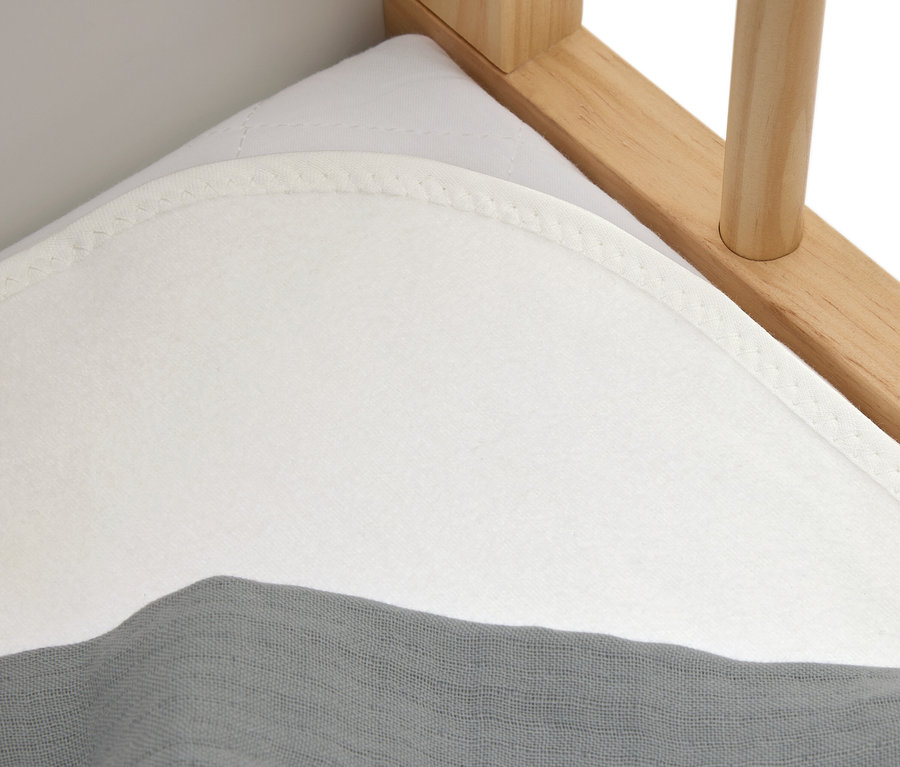 Nahaufnahme einer weißen Matratze mit einem grauen Tuch auf einem Holzbett.