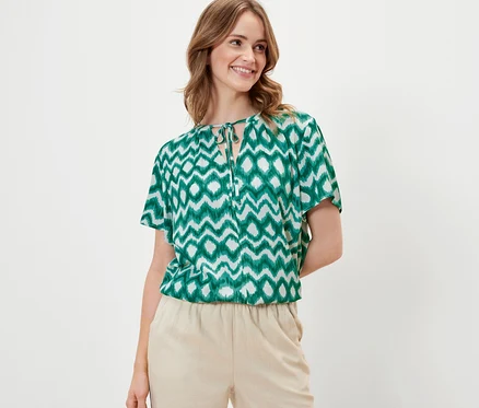Frau trägt eine bedruckte Tunika-Bluse und eine beige Hose.