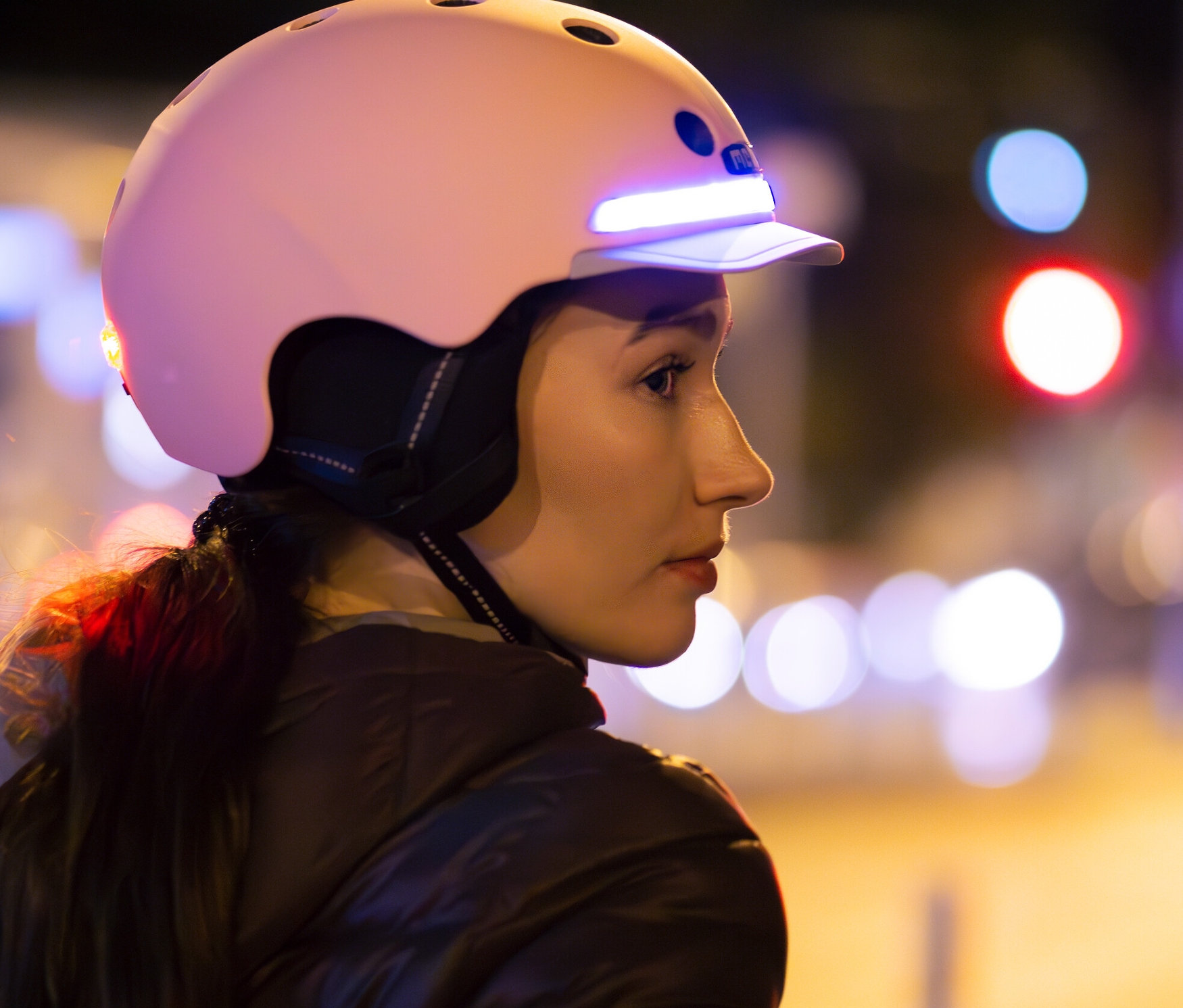Frau mit braunen Haaren trägt einen hellrosa Melon E-Series Fahrradhelm »Lotus« auf dem Kopf.