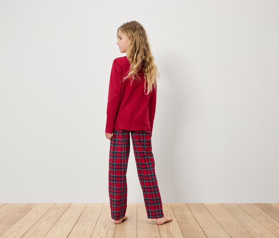 Ein Mädchen in einem roten Schlafanzug mit karierter Hose steht mit dem Rücken zum Betrachter.
