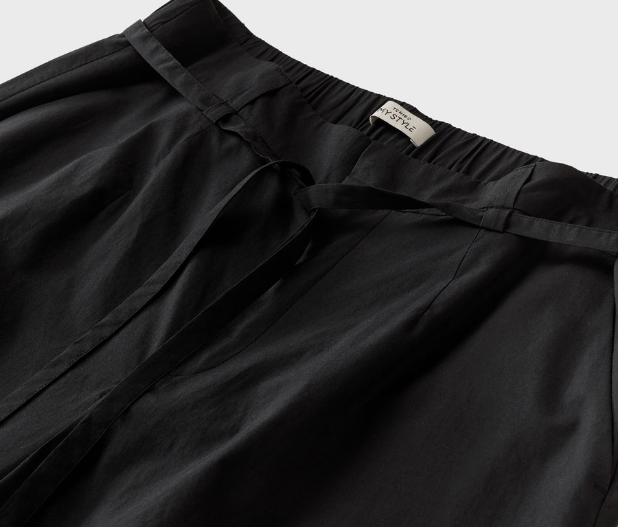 Detailaufnahme einer schwarzen Hose mit Bindegürtel und einem Etikett mit der Aufschrift "TCHINO MY STYLE".