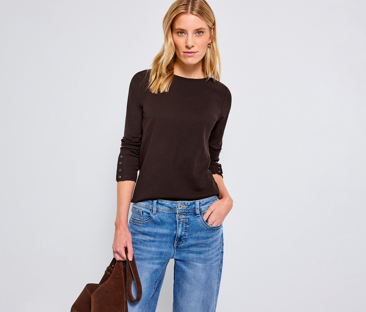 Frau trägt ein braunes Street One Rippshirt, blaue Jeans und hält eine braune Tasche.