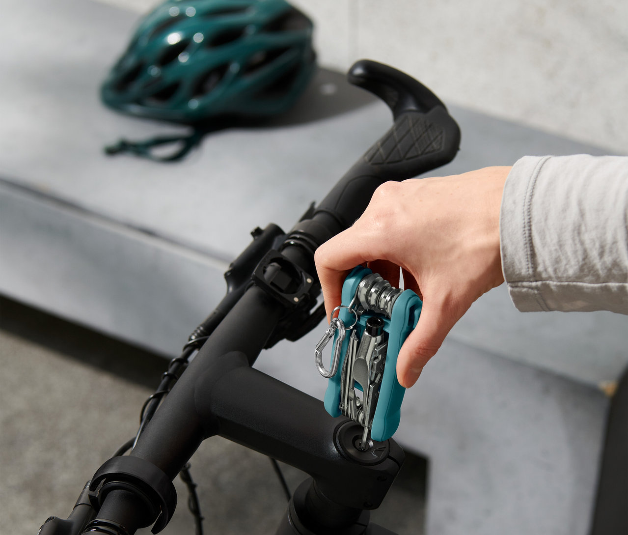 Hand befestigt Multifunktionswerkzeug am Fahrradlenker, im Hintergrund Fahrradhelm.