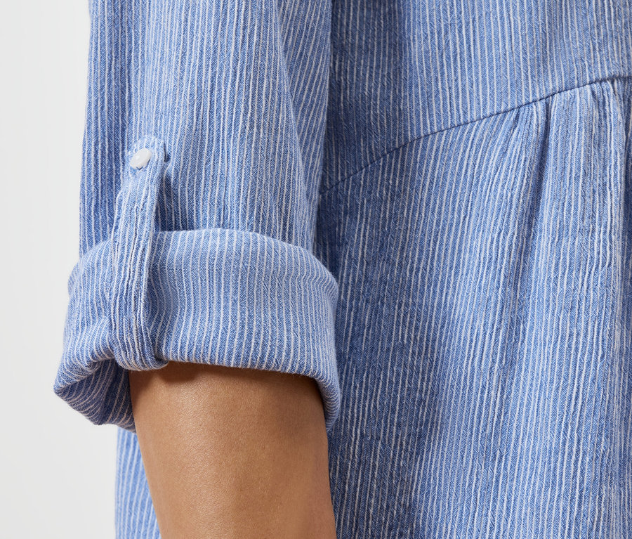 Nahaufnahme eines hochgekrempelten Ärmels eines blau-weiß gestreiften Hemdes.