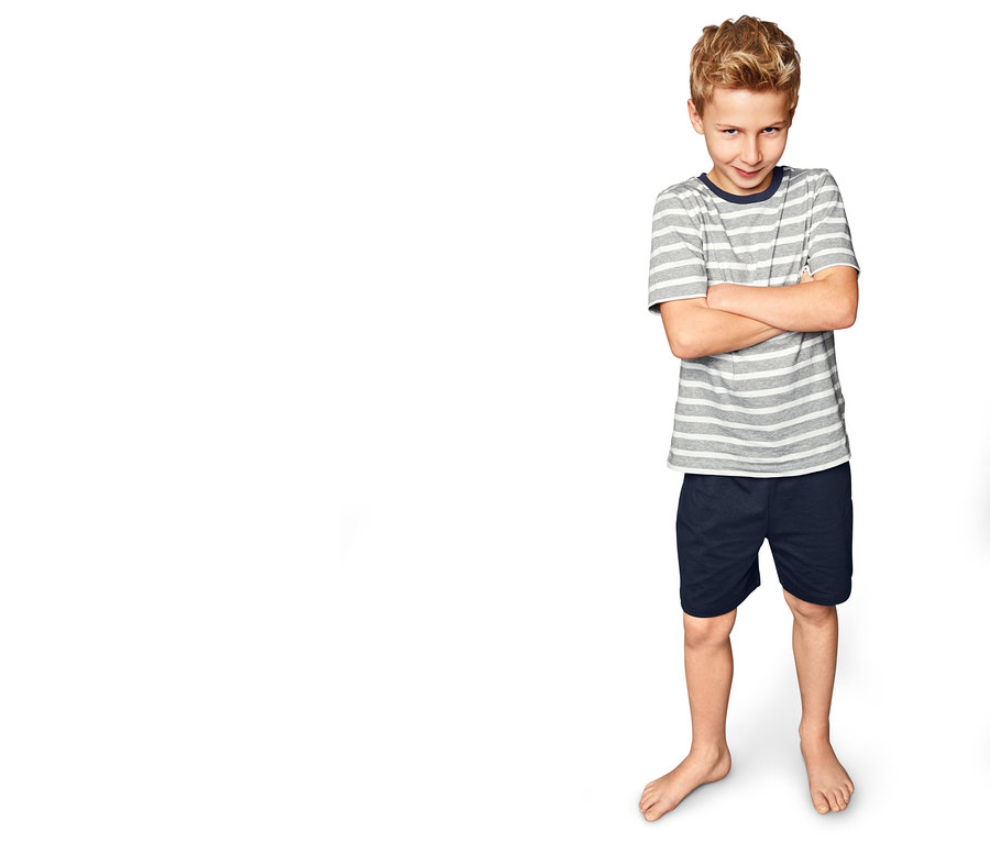 Junge steht mit verschränkten Armen vor weißem Hintergrund. Er trägt einen Jungen-Shorty-Pyjama.