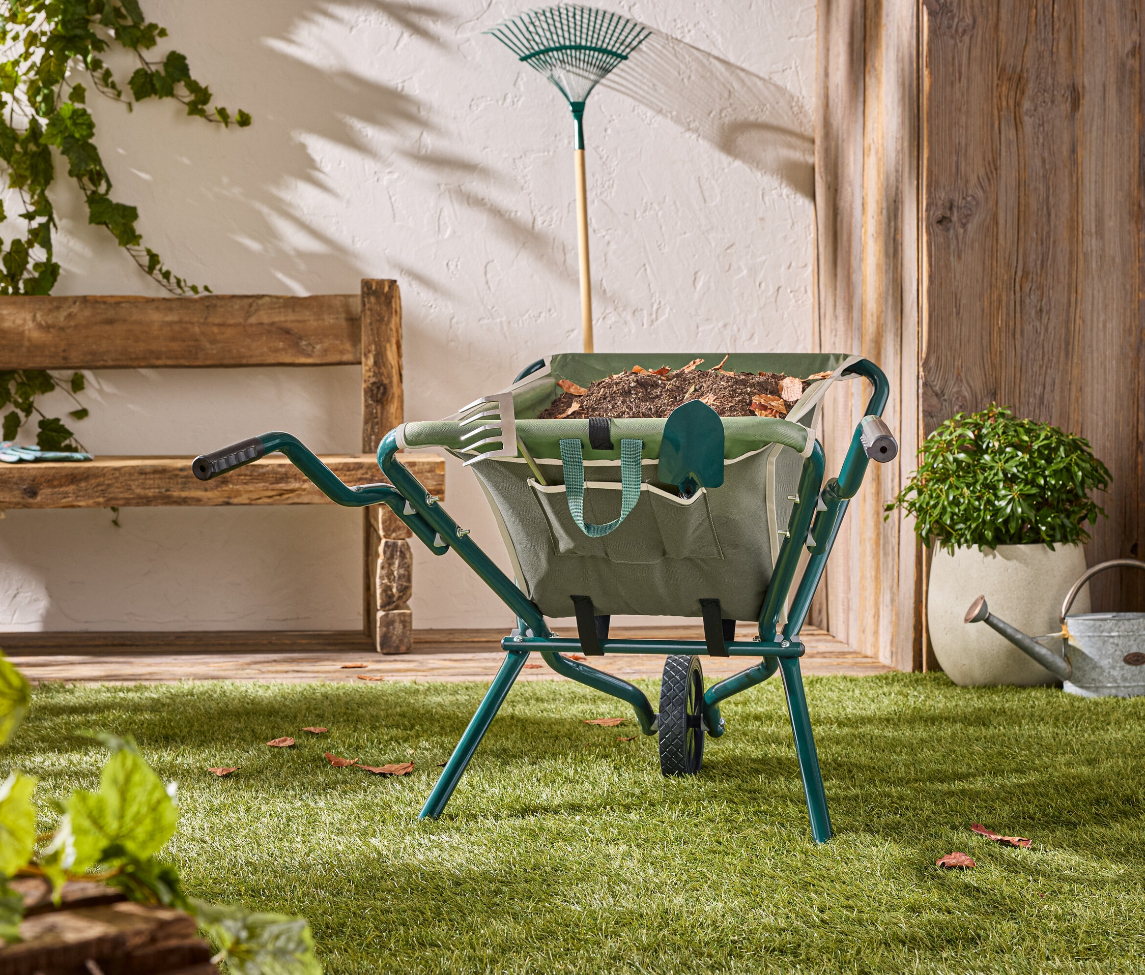 Eine grüne Schubkarre steht auf einem Rasen mit Gartenwerkzeugen darin.