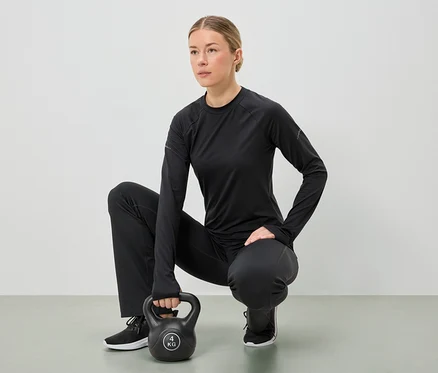 Eine Frau in schwarzer Sportbekleidung hockt und hält eine 4-kg-Kettlebell mit beiden Händen.