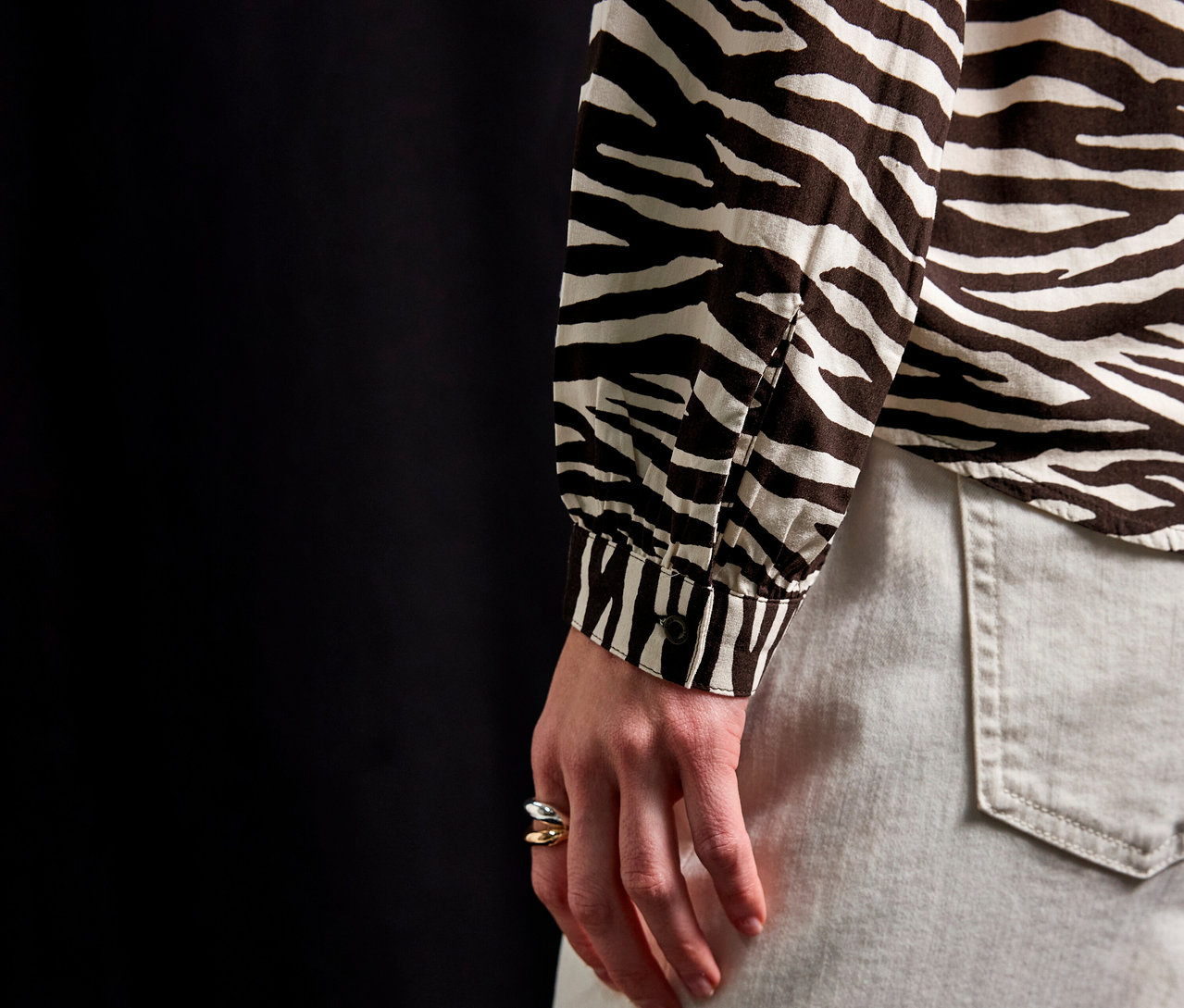 Nahaufnahme einer Person, die eine Street One Bluse mit Zebra-Muster und helle Jeans trägt.