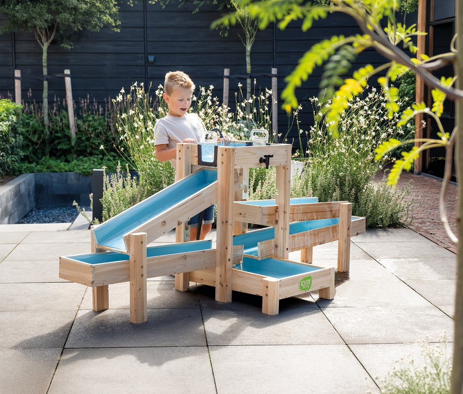 Ein Junge spielt mit einem hölzernen Wasserspielplatz mit blauen Rinnen im Garten.