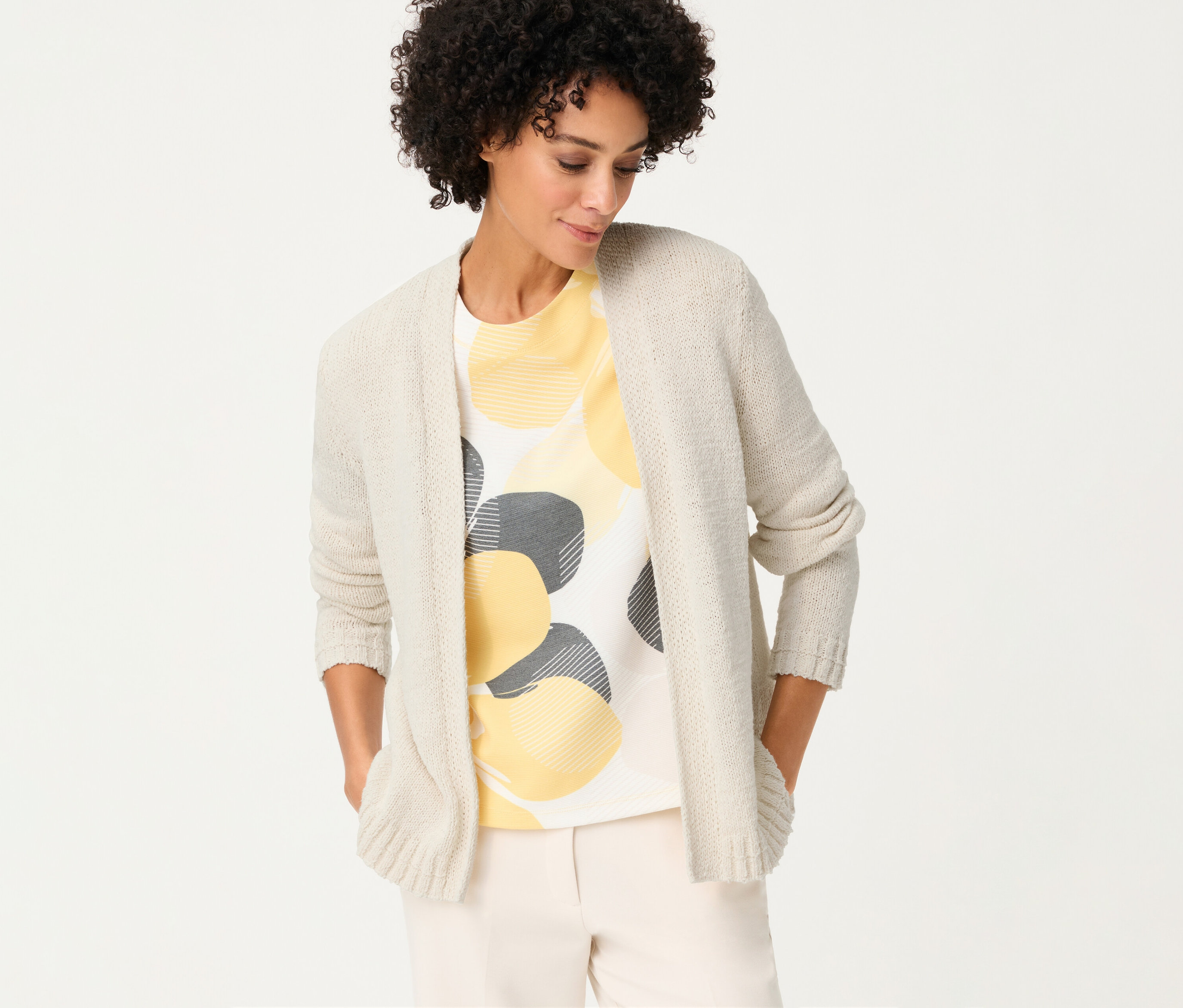 Frau mit Olsen Leinen-Cardigan über einem T-Shirt mit gelben und grauen Kreisen, die ihre Hände in den Taschen hat.