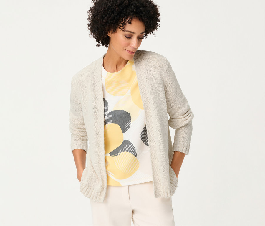 Frau mit Olsen Leinen-Cardigan über einem T-Shirt mit gelben und grauen Kreisen, die ihre Hände in den Taschen hat.
