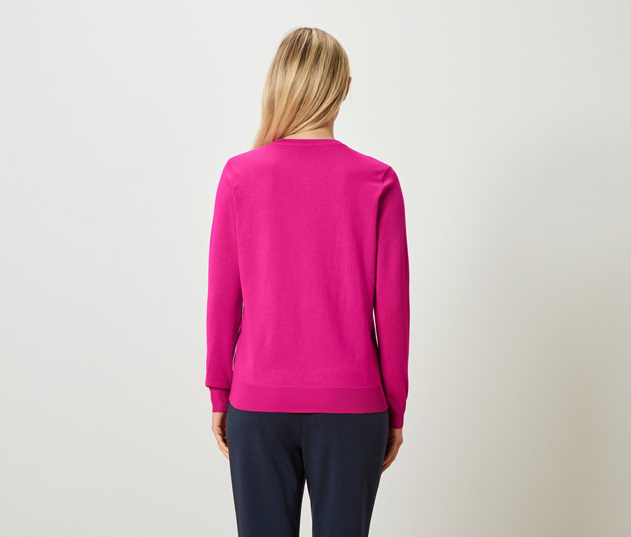 Rückansicht einer Frau mit blonden, hochgesteckten Haaren, die einen pinkfarbenen Pullover und marineblaue Hosen trägt.