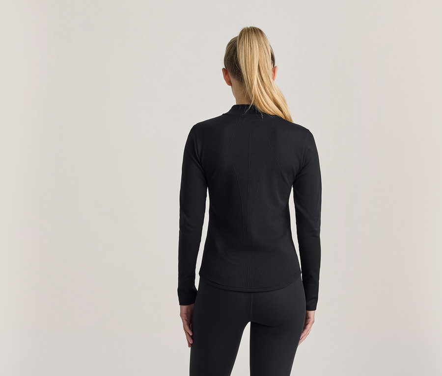 Frau von hinten, mit blonden Haaren im Pferdeschwanz, trägt ein schwarzes Langarmshirt und schwarze Leggings.