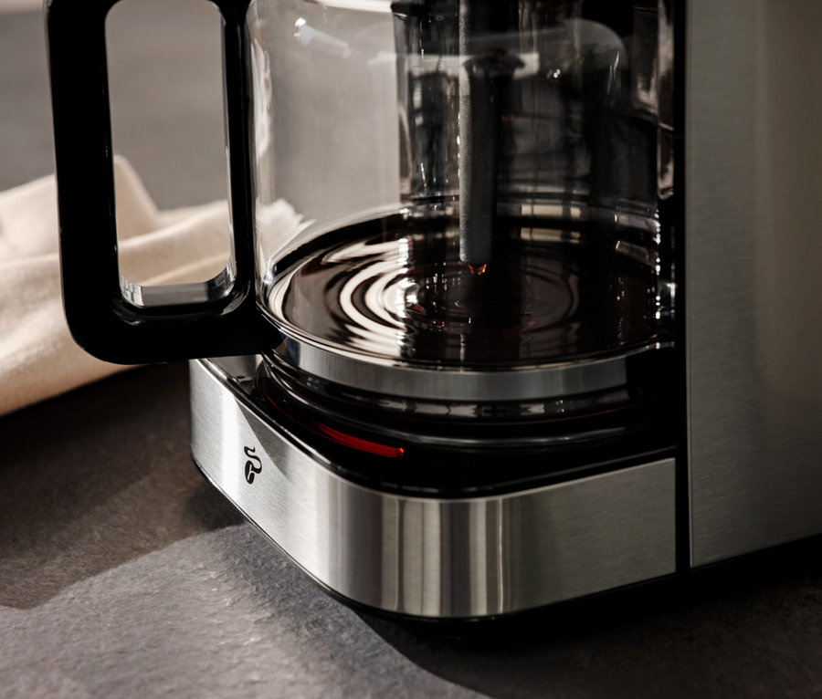 Detailansicht einer Kaffeemaschine mit Kaffeekanne und einem beigen Tuch im Hintergrund.
