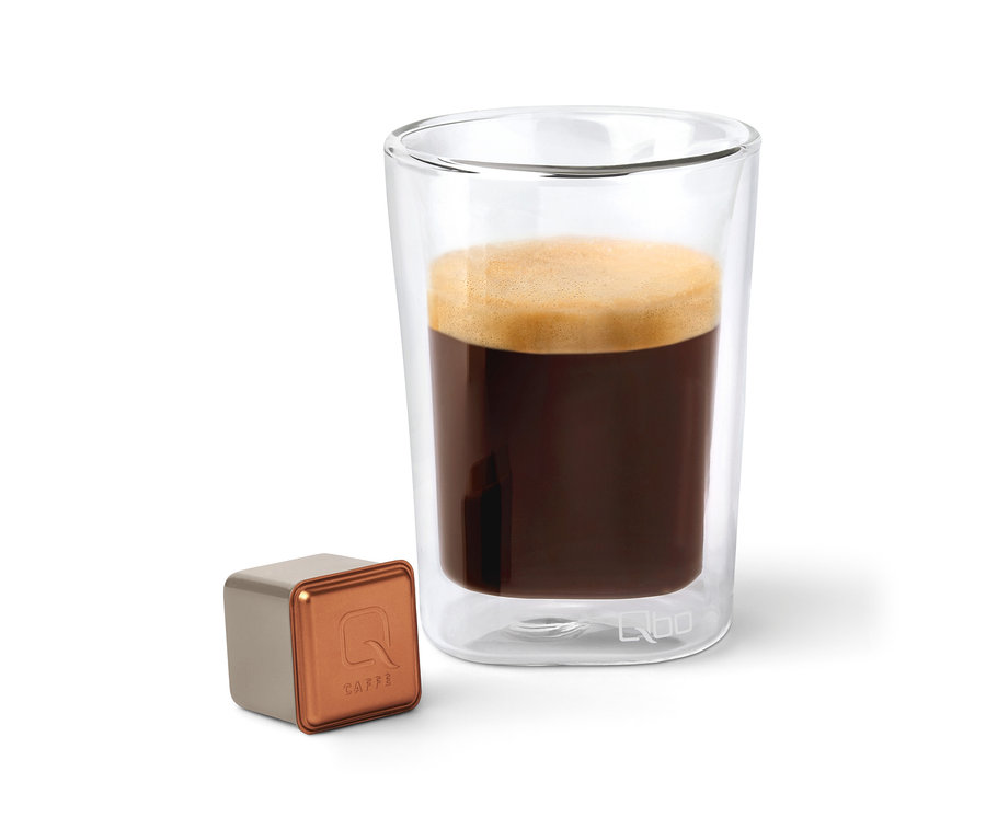Eine Qbo Caffè BUNA ENTETA Kapsel neben einem Glas Kaffee.