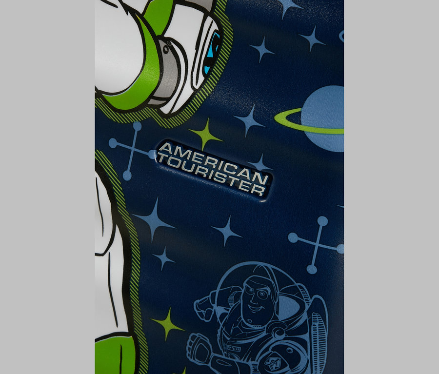Nahaufnahme eines dunkelblauen Koffers mit Weltraum-Motiv. Er zeigt ein silbernes „AMERICAN TOURISTER“-Logo, eine große Grafik von Buzz Lightyears Kopf und Schulter links und eine kleinere Umrisszeichnung von Buzz Lightyear rechts unten, umgeben von Sternen, Planeten und geometrischen Symbolen.