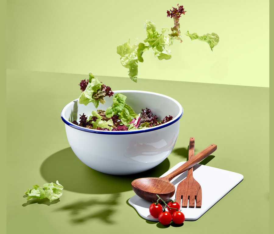 Grüner Salat in Servier- und Zubereitungsschüssel mit Holzbesteck und Tomaten.