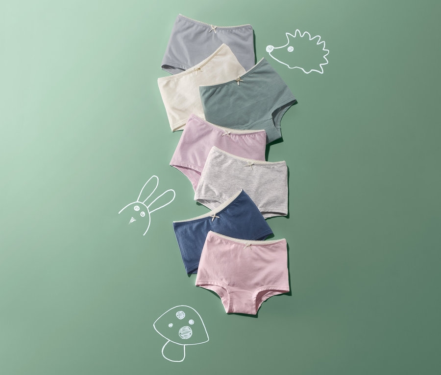 Auf grünem Hintergrund liegen 7 Mädchen-Pantys in verschiedenen Farben übereinander.
