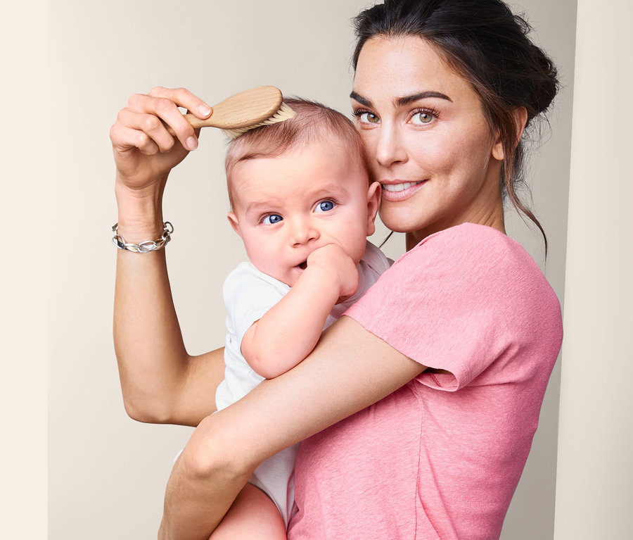Frau hält Baby und bürstet seine Haare mit einer Baby-Naturhaarbürste.