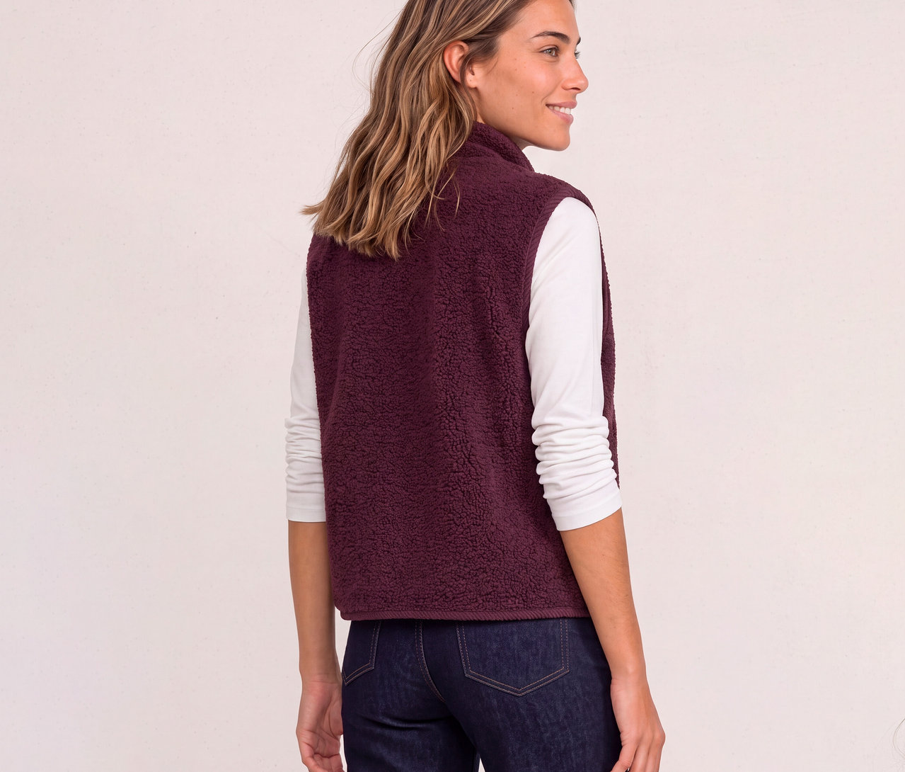Frau trägt eine rote Street One Fleece-Weste über einem weißen Langarmshirt und Jeans, blickt über die Schulter.