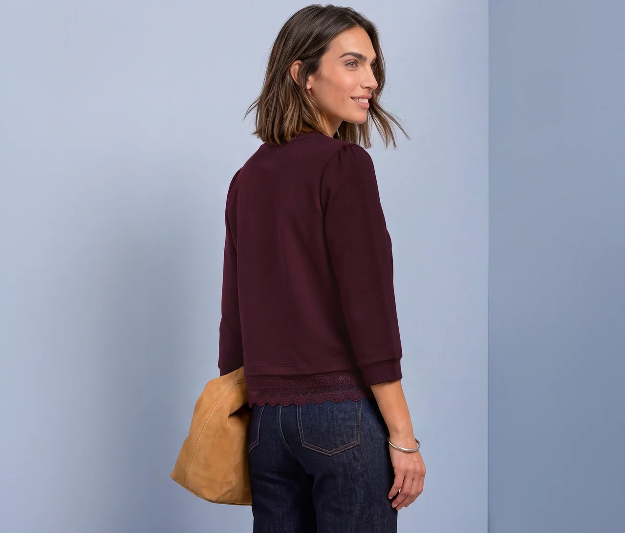 Frau trägt ein rotes Street One 3/4-Jerseyshirt mit Spitzenborte, dunkle Jeans und eine braune Tasche, blickt über die Schulter.