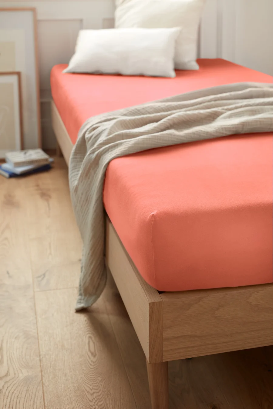 Korallefarbenes Jersey-Spannbettlaken in Normalgröße auf einem Bett mit weißen Kissen und Überwurf.