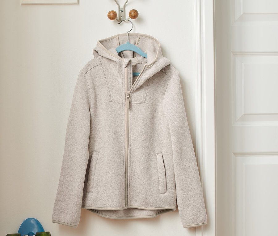 Eine beige Strickfleece-Jacke hängt an einer Garderobe neben einem blauen Skateboard.