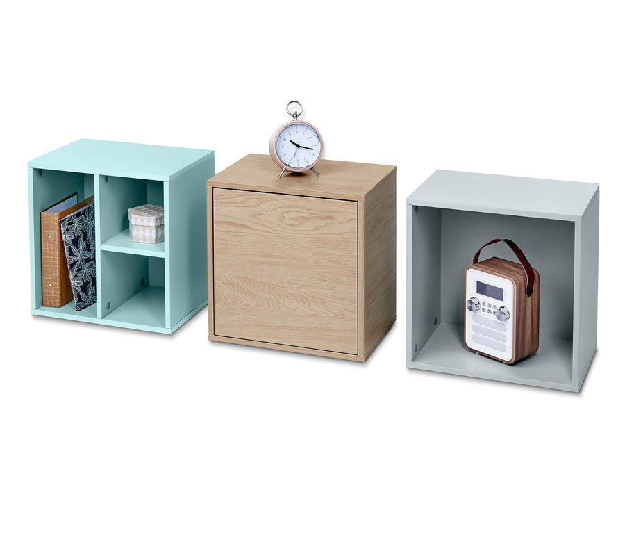 Drei Modulwürfel in Blau, Holz und Grau. Im blauen Würfel befinden sich Ordner, auf dem Holzwürfel steht ein rosa Wecker und im grauen Würfel befindet sich ein Radio.
