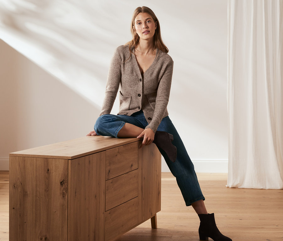Frau sitzt auf Kommode und trägt Jeans in verkürzter Länge.