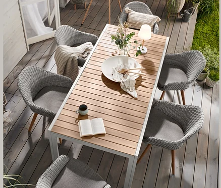 Auf einer Gartenterrasse steht ein Ausziehtisch »Liska« aus Aluminium, umgeben von Schalenstühlen mit Polyrattangeflecht. Im Hintergrund eine LED-Akku-Stehleuchte in Holzoptik und beige und hellgraue Blumentöpfe mit Füßen.