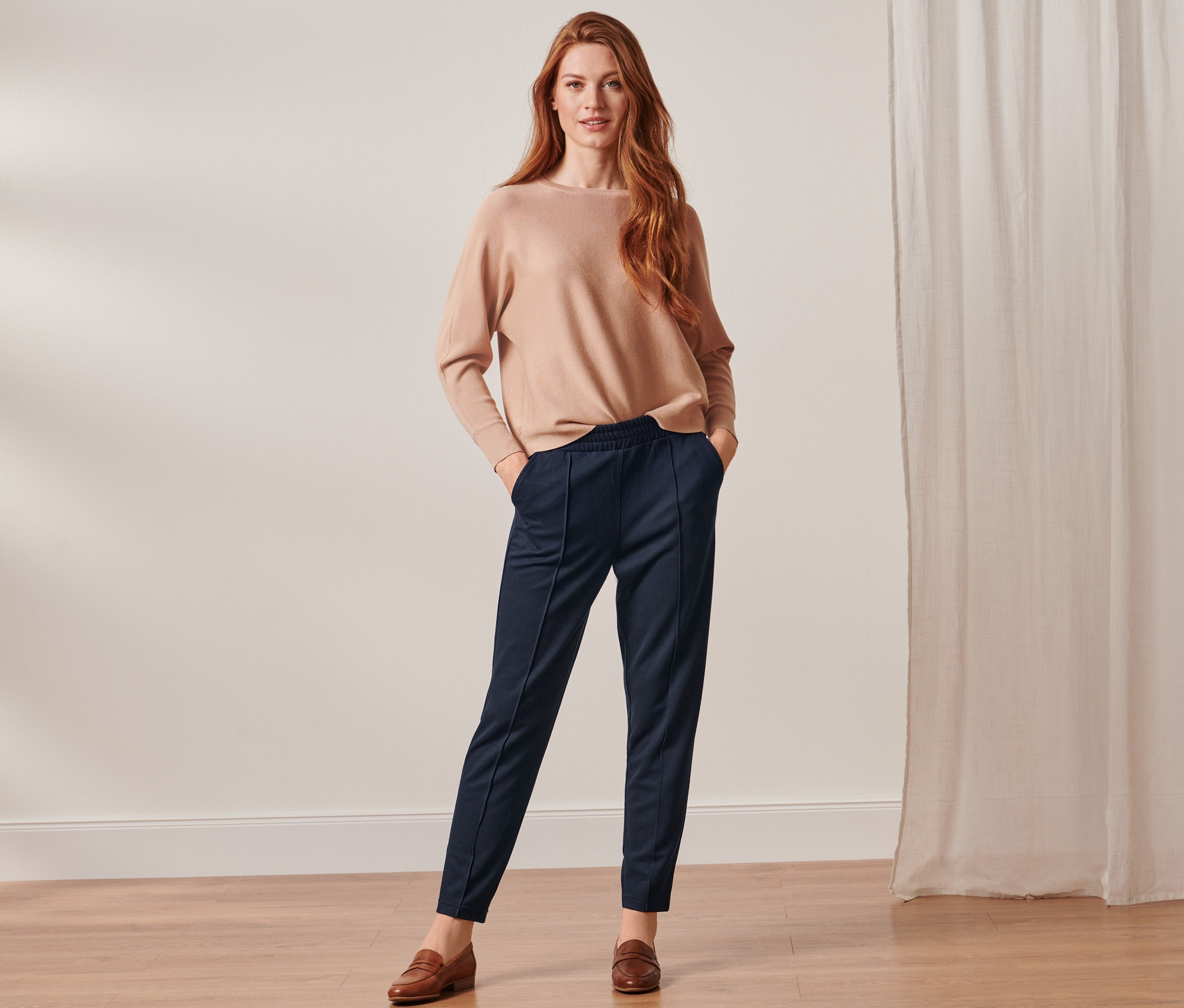 Frau posiert in beigem Pullover und dunkelblauer Joggpants mit Biese.