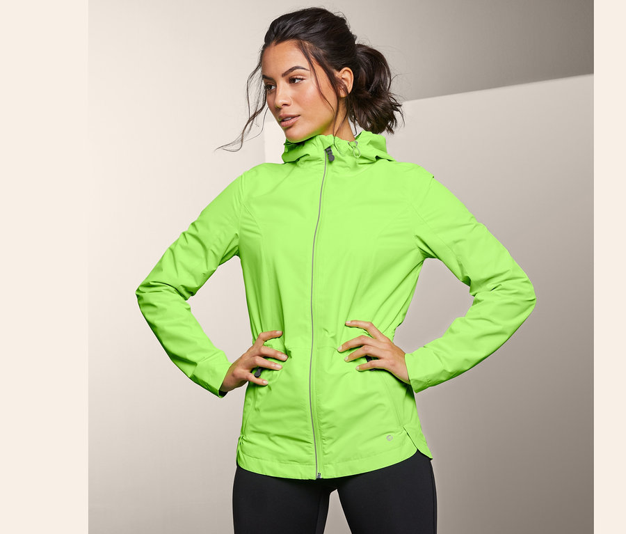 Frau posiert in neongrüner Windprotection-Laufjacke.