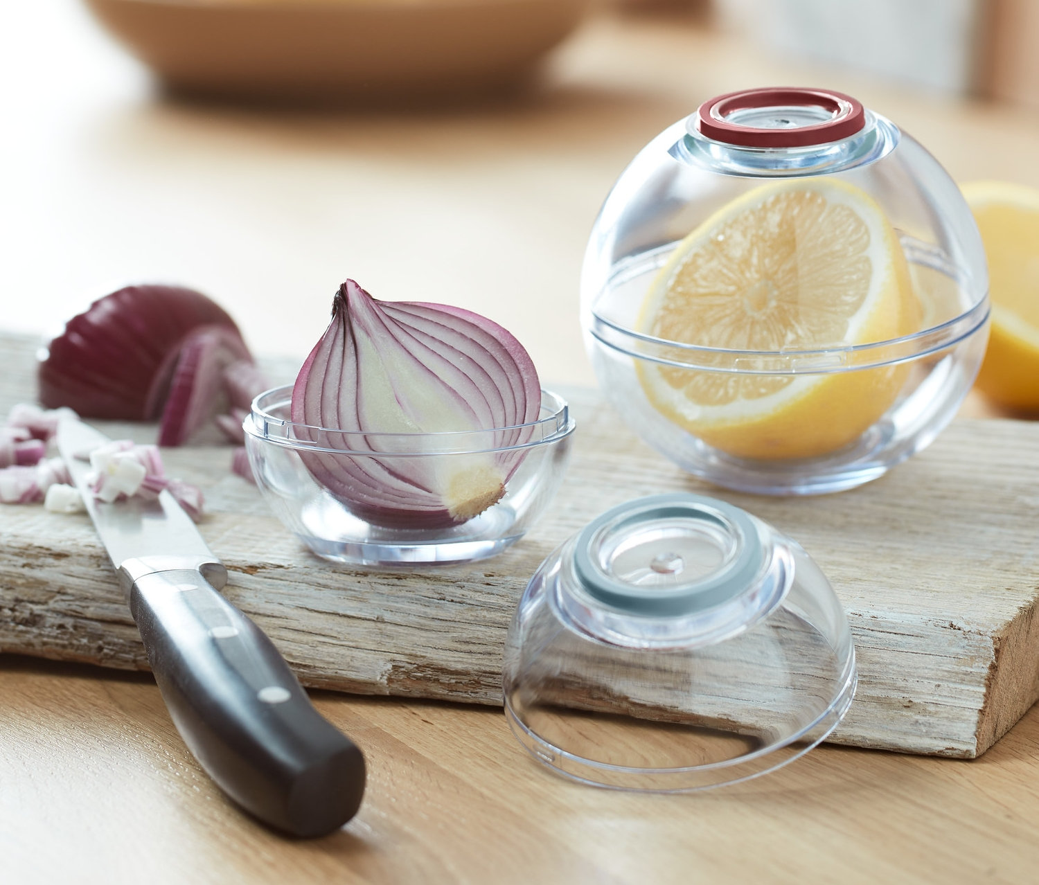 Geschnittene Zwiebel und Zitrone in 2 Frischhaltekugeln auf einem Holzbrett mit Messer.