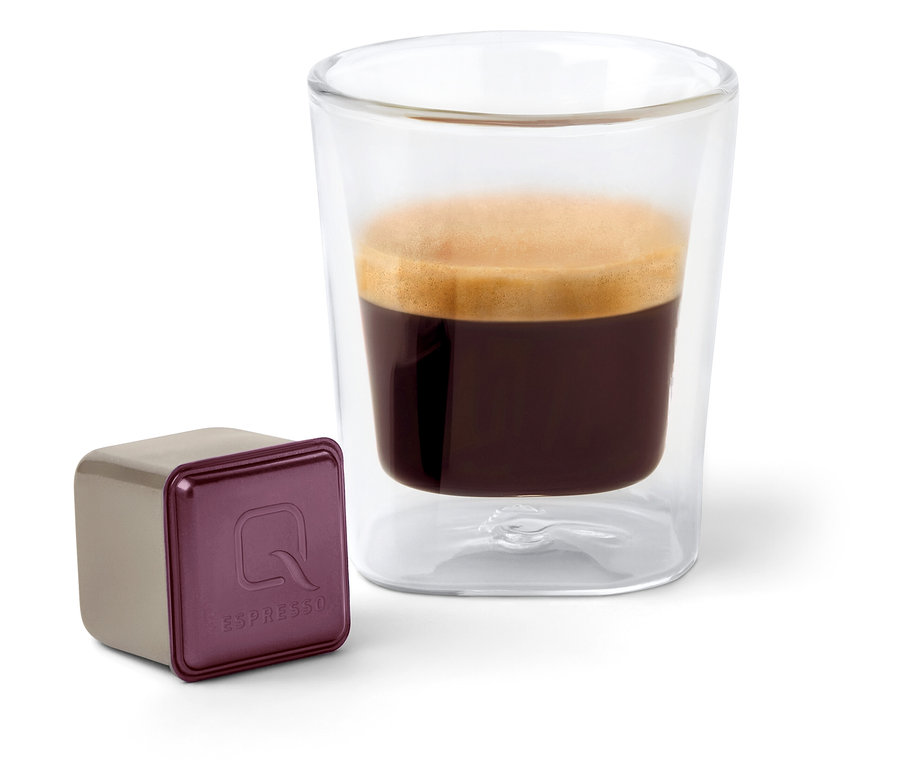 Eine Qbo Espresso ORO TOLIMA Kapsel neben einer Tasse Espresso.