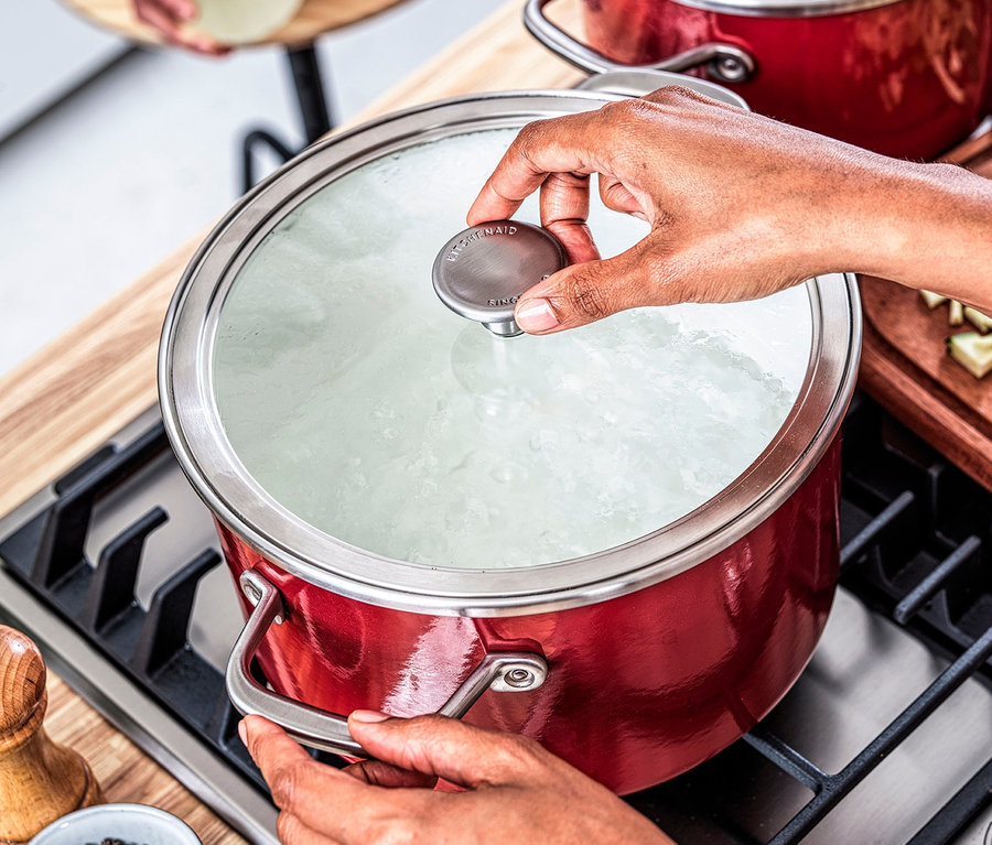 Eine Frau kocht in einem roten KitchenAid Steel Core Enamel Kochtopf mit Deckel.