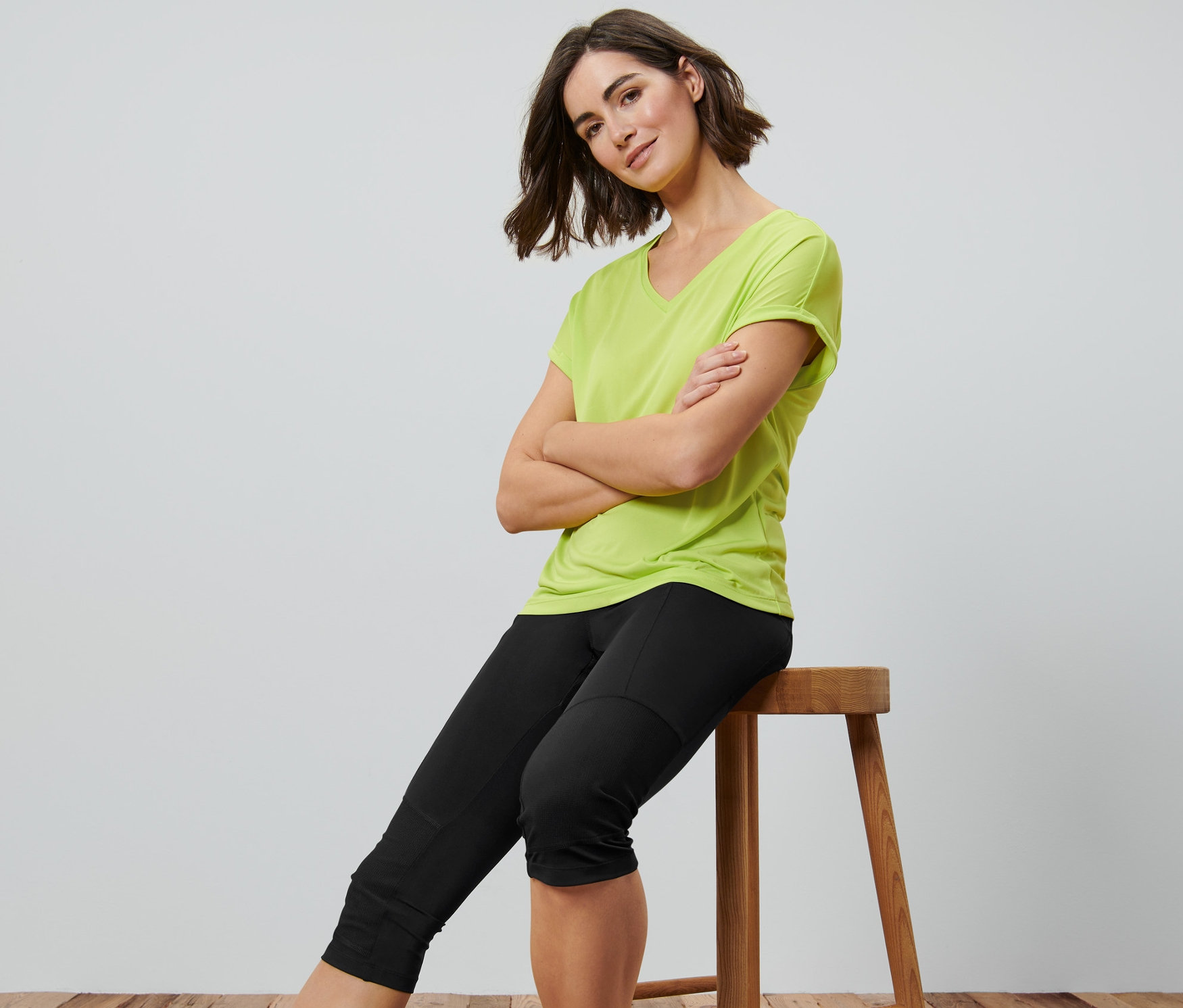 Frau sitzt mit verschränkten Armen auf einem Hocker und trägt eine schwarze 3/4-Trekking-Tight.